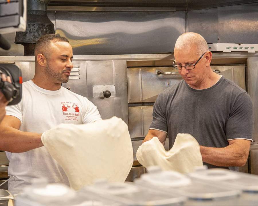 Pietro and Robert Irvine stretching pizza dough