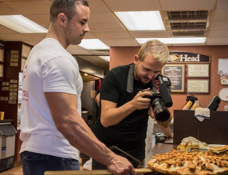 A photographer shooting a breakfast pizza while Pietro plates it