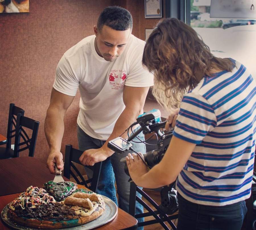 Pietro cutting a dessert pizza while a camera operator films